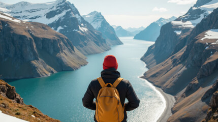 Person stands mountain overlooking stunning valley with river winding through it, surrounded by snow capped peaks. scene evokes sense of adventure