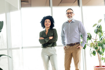 Confident coworkers standing in a modern office space showcasing diverse teamwork and professional...