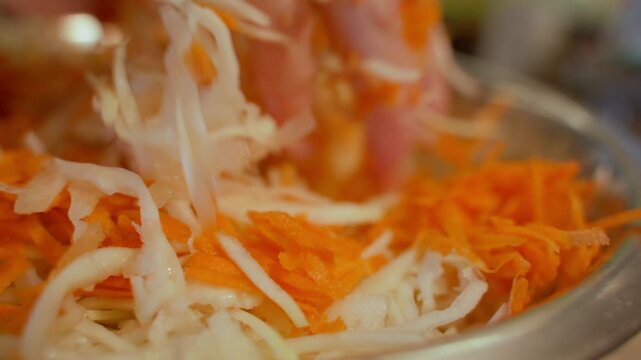 Close-up of shredded carrots and cabbage mixing by hand 