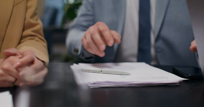A business man and a woman sign a contract sitting at a desk in an office. Close-up of their hands, unrecognizable persons