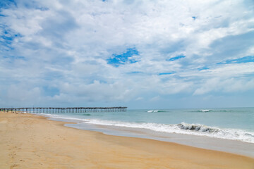 Wooden Pier over Atlantic Ocean. Scenic beach view with clouds and surf.