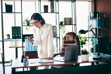 Charming businesswoman in formal suit working on tasks during office hours by multitasking with her...
