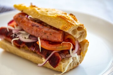 Traditional Argentine sandwich known as choripan prepared with roasted chorizo, chimichurri, cabbage, tomato, onion and sourdough bread. Real food