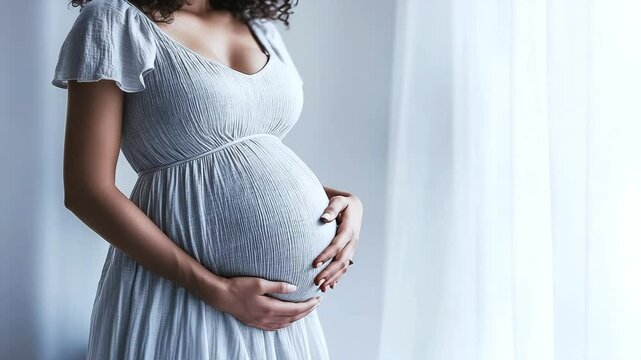Pregnant woman in gray dress hugs belly on gray background. Expecting baby, concept of motherhood and childhood. Healthy, happy pregnancy
