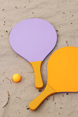 Beach tennis rackets and ball on sand. Active lifestyle, games and sports. Beach tennis set. Bright wooden rackets for outdoor games. Summer outdoor games. Summer sports and games concept. Close-up