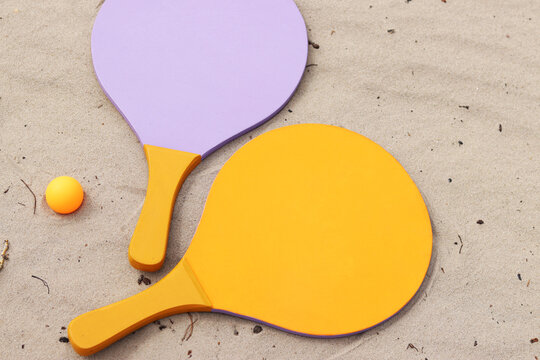Beach tennis rackets and ball on sand. Active lifestyle, games and sports. Beach tennis set. Bright wooden rackets for outdoor games. Summer outdoor games. Summer sports and games concept. Close-up