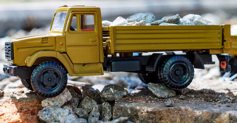 A vibrant yellow toy dump truck, brimming with small, realistic stones, navigates a miniature...