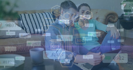 Couple sitting on tufted couch at home, reviewing laptop data with mug and digital overlay graphics