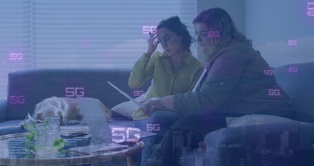 Reviewing papers and typing on laptop two women sitting on living room couch, with sleeping dog
