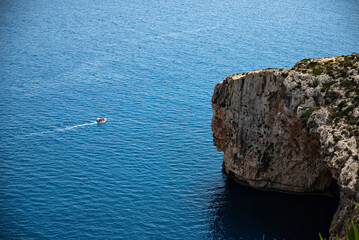A small tourist boat sails past rocks and a natural arch