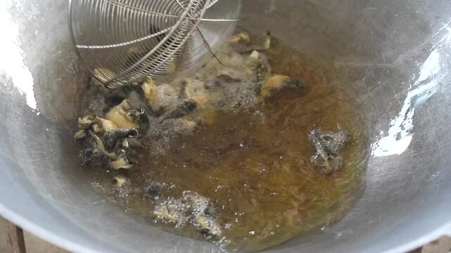 Traditional cooking method of frying frog skin in a pan with oil