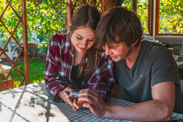 A teenage couple, a boy and a girl, are sitting at a table and looking at a smartphone, a date...