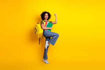 Happy young student holding book and celebrating success with a gesture on a vibrant yellow...