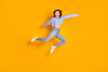 Fototapeta premium Cheerful young fashion model jumping against a vibrant yellow background wearing a stylish casual outfit