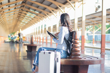 A young Asian woman stands on a public transport platform, holding a map, smiling slightly. She...