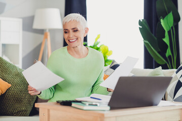 Mature woman at home with documents and laptop, enjoying leisure time in comfortable indoor setting