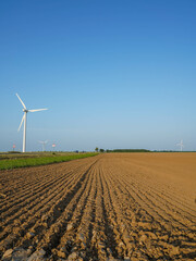 Plowed soil stretches across a field with wind turbines on the horizon