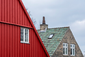 Red wooden facade next to classic green tile roof house in Christianshavn, Copenhagen, Denmark, traditional Danish construction and architectural heritage