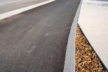 Curved border between asphalt road and light concrete pavement with mulch, minimal urban detail and clean geometry