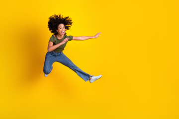 Obraz premium Cheerful young woman jumping in excitement against bright yellow background, showcasing joy and vitality in casual attire