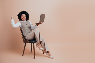 Confident businesswoman sitting on a chair with a laptop, expressing motivation and success in a...