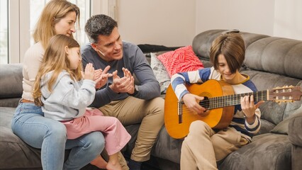 Family enjoying music at home: teenage boy playing guitar for his clapping family
