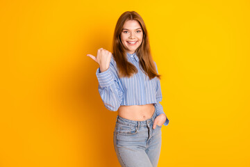 Smiling young woman pointing confidently against a yellow background in casual trendy outfit -...