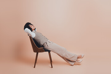 Confident young businesswoman in elegant formal attire reclining on chair against a soft beige...