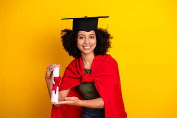 Confident graduate young woman holding her diploma against a vibrant yellow background celebrating...