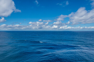 Obraz premium Vast Azure Horizon Mid-Day Seascape with Gentle Waves, Puffy Cumulus Clouds, and Dramatic Sky-Ocean Contrast in Sunlit Clarity