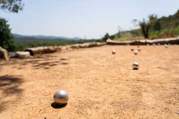 A beautiful scene of a petanque game being played outdoors, with metal balls scattered over a sandy court under the sun