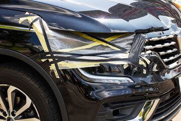 A black car that has a damaged bumper and a broken headlight