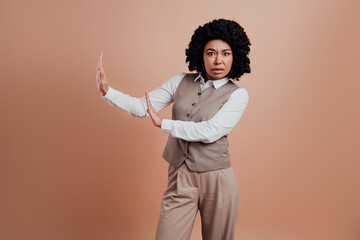 Confident young businesswoman making a hand gesture against a beige background, wearing formal attire with stylish professionalism