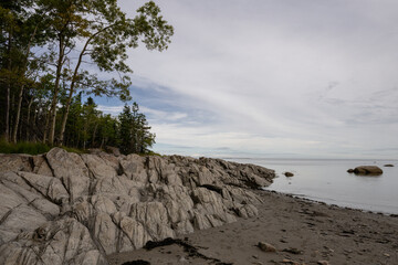 view from the rocky beach of a lake shore with a calm lake under a cloudy sky in summer