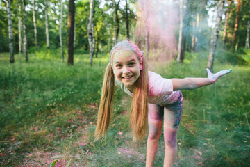 Happy Caucasian child with colorful holi powder on face and clothes smiles and bends forward with...