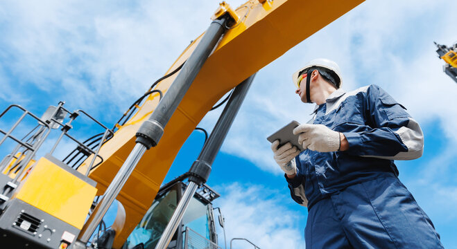 Male engineer mechanic with tablet inspecting mining machinery under blue sky - Powered by Adobe