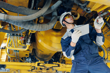 Male engineer examining mining machinery with tablet in industrial setting