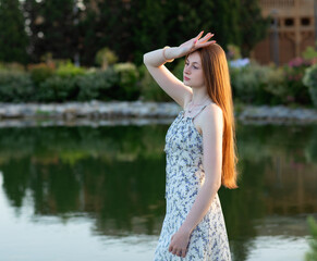 Young woman in a floral dress enjoys a peaceful travel moment by a lake, soaking in nature and sunshine. Perfect concept for summer journeys and slow living