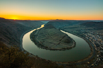 Sunrise over the Moselle. The river winds through a valley in a narrow loop surrounded by vineyards...