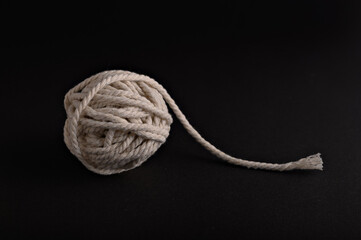 A ball of rope sits on a dark surface, featuring a loose end that drapes outwards, creating an...