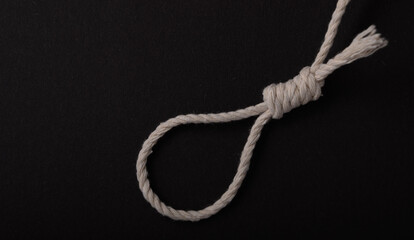 A natural fiber rope is tied in a loop knot, resting on a dark surface, demonstrating a clean and...