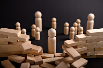 Wooden figures are positioned around a broken wall, with blocks spread on a dark surface,...