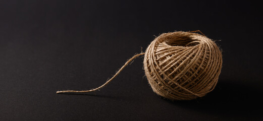 A ball of jute string sits on a dark surface, displaying its intricate loops and natural fibers,...