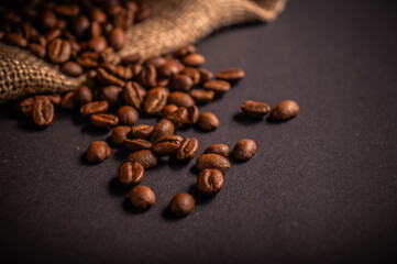 Rich, dark roasted coffee beans spread across a black surface next to burlap fabric, evoking the essence of freshly brewed coffee