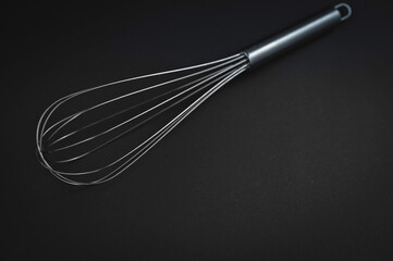 A stainless steel whisk is positioned on a dark surface, highlighting its functional design for...