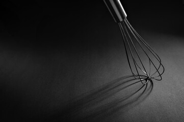 A metal whisk lies on a matte black surface, creating delicate shadows that enhance the simplicity of kitchen tools