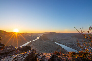 Sunrise over the Moselle. The river winds through a valley in a narrow loop surrounded by vineyards...