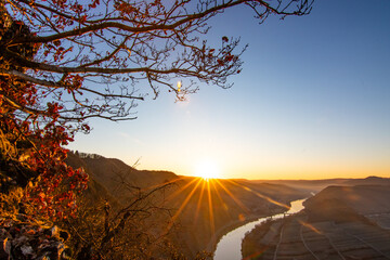 Sunrise over the Moselle. The river winds through a valley in a narrow loop surrounded by vineyards...