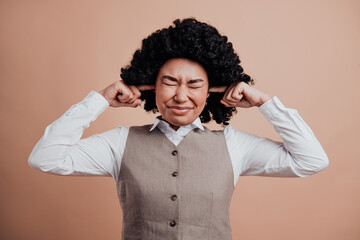 Confident businesswoman in formal attire covering her ears with fingers against soft beige...