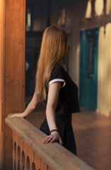 Young woman stands on a wooden balcony, gazing toward a door bathed in warm light. A symbolic moment of dreams, inner desires, and stepping into the future